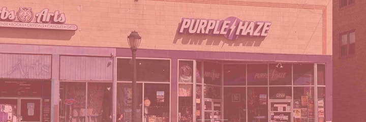 A storefront with signs "Purple Haze" and "Arts" featuring decor items, books, crystals, and gifts.
