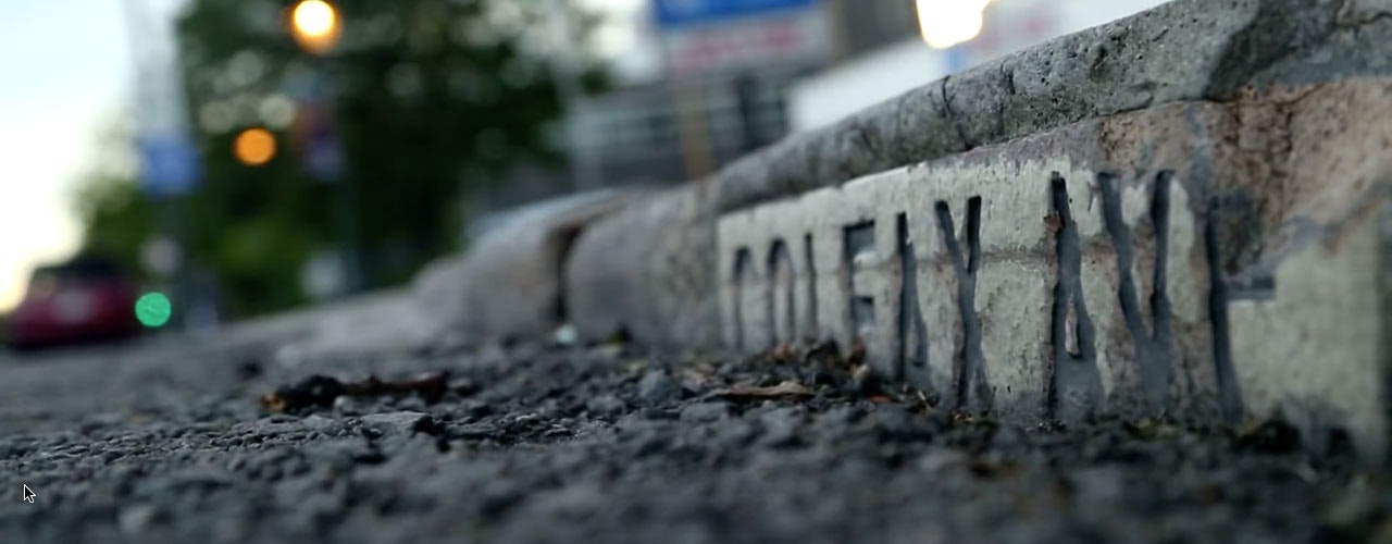 A close-up of a curb with the engraved text "COFEY AVE," surrounded by a blurred street scene.