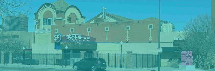 Street view of "The Fillmore Auditorium" building with a car parked in front and trees around.