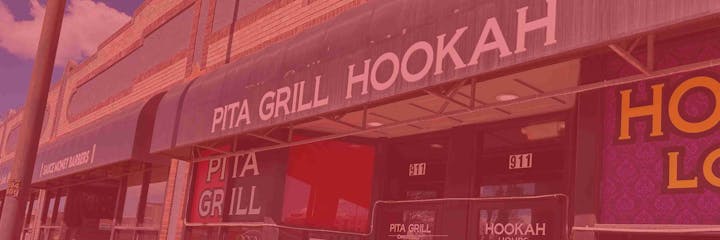 Storefronts with signs for "Pita Grill Hookah" and "Sauce Money Barbers", in a brick building.