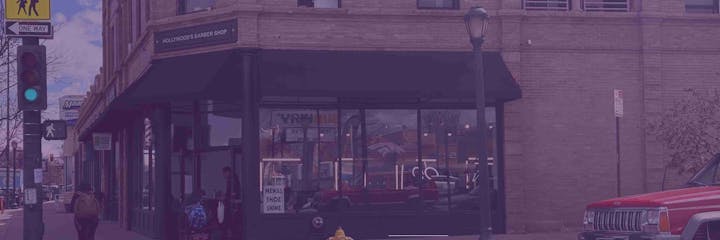 Street corner with a barbershop, pedestrian, traffic light, and a red SUV parked nearby.