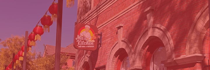 A brick building with a sign for "Ma's Kitchen," featuring dim sum and noodles, decorated with red lanterns.