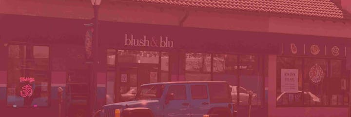 Storefront of "blush & blu" with a parked Jeep in front, signs, and a neon light.