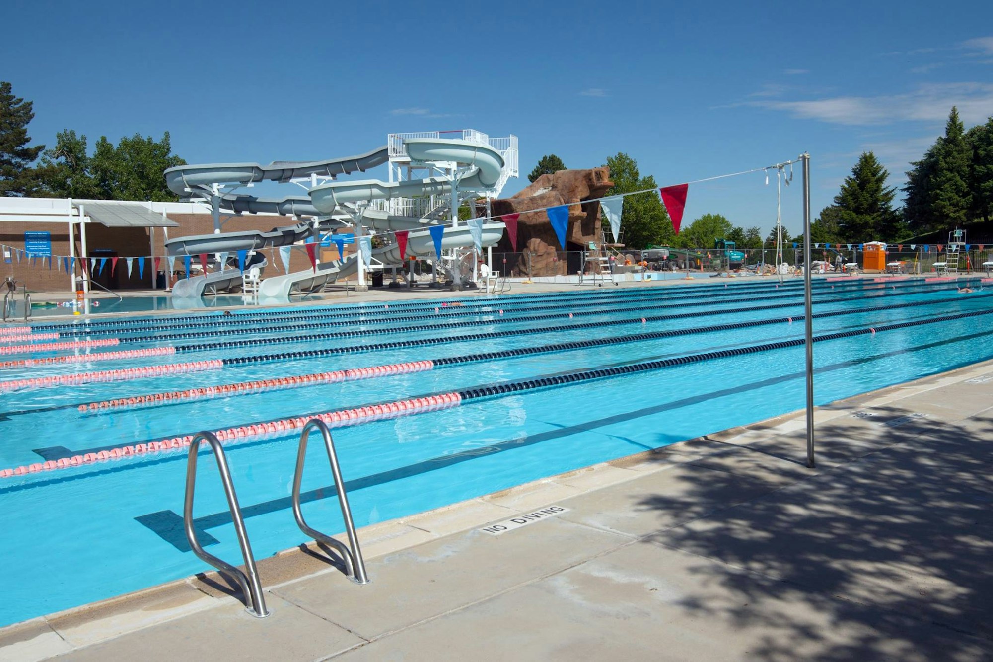 Outdoor swimming pool with lanes, water slides, and bunting flags.