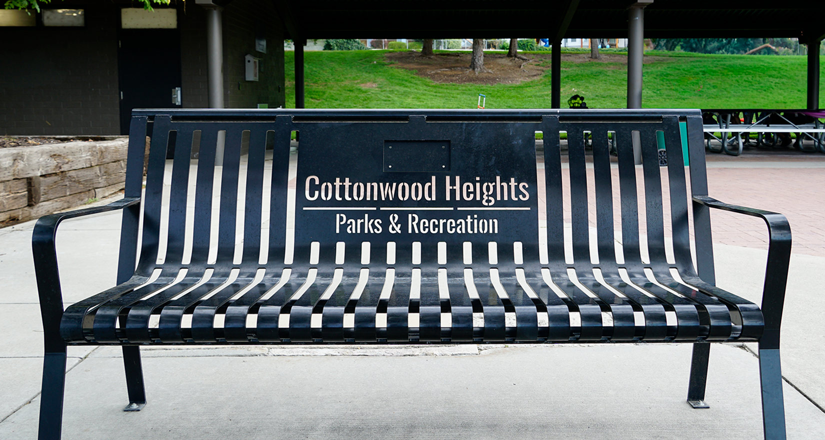 A black metal bench with "Cottonwood Heights Parks & Recreation" printed on it.