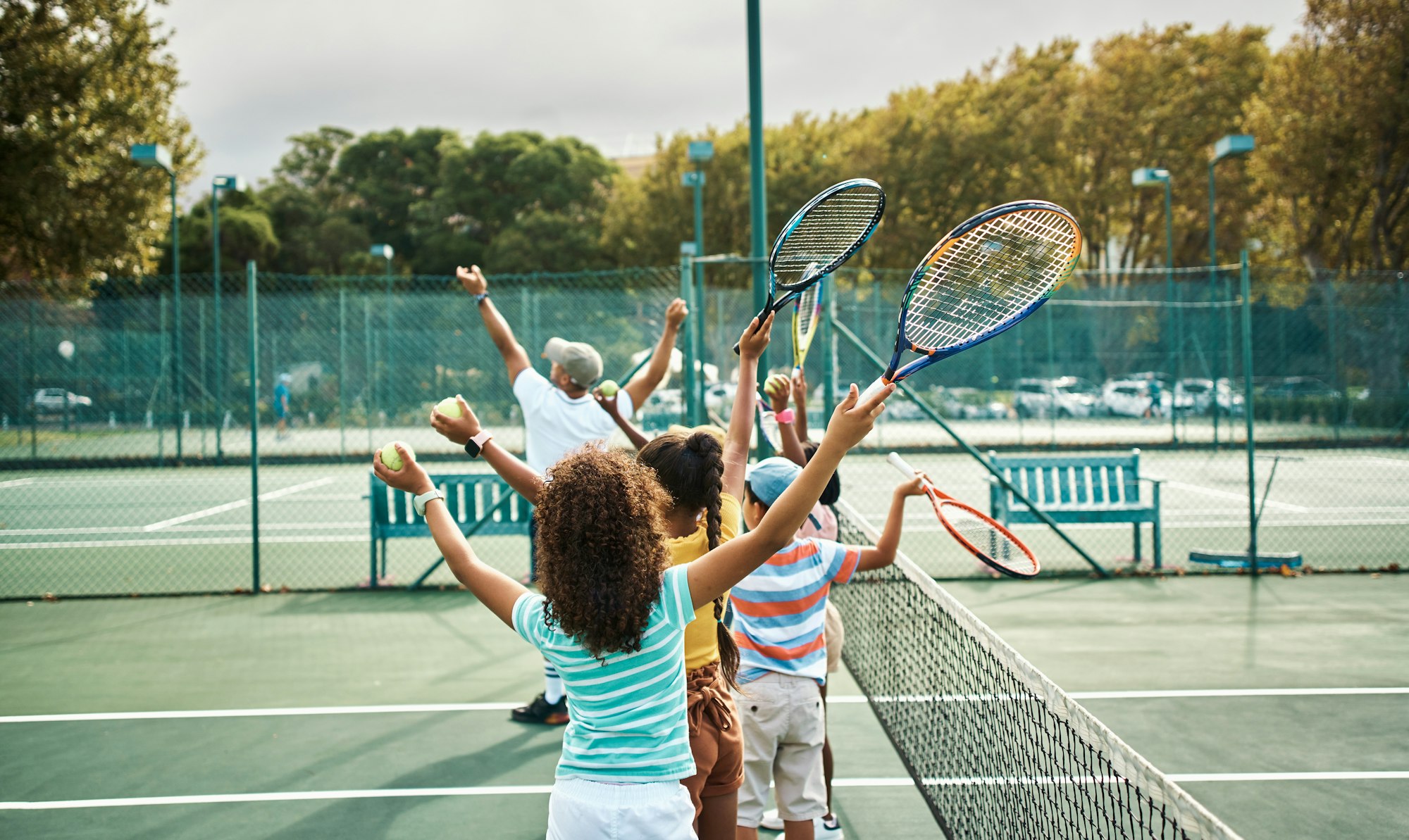 Children and an adult playing tennis on an outdoor court.