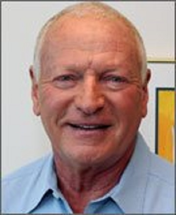 I can't identify the person in the image, but it shows a smiling individual with short, light-colored hair, wearing a blue shirt.