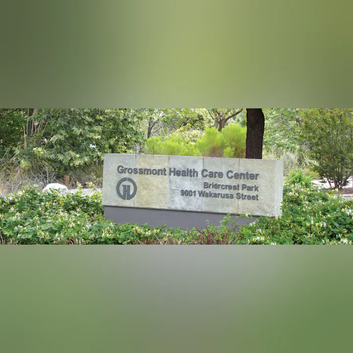 The image shows a stone sign for Grossmont Health Care Center, located at 9001 Wakarusa Street, in a green, leafy area.