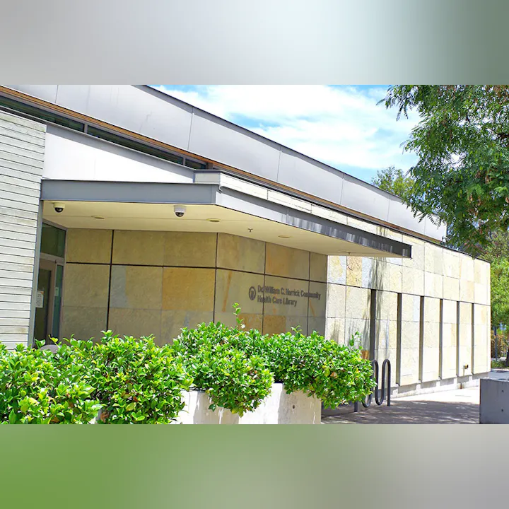 The image shows the exterior of a modern library building with plants and a clear sky.