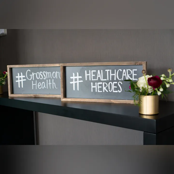 The image features two signs: one says "#Grossmont Health" and the other "#HEALTHCARE HEROES," alongside a small floral arrangement.