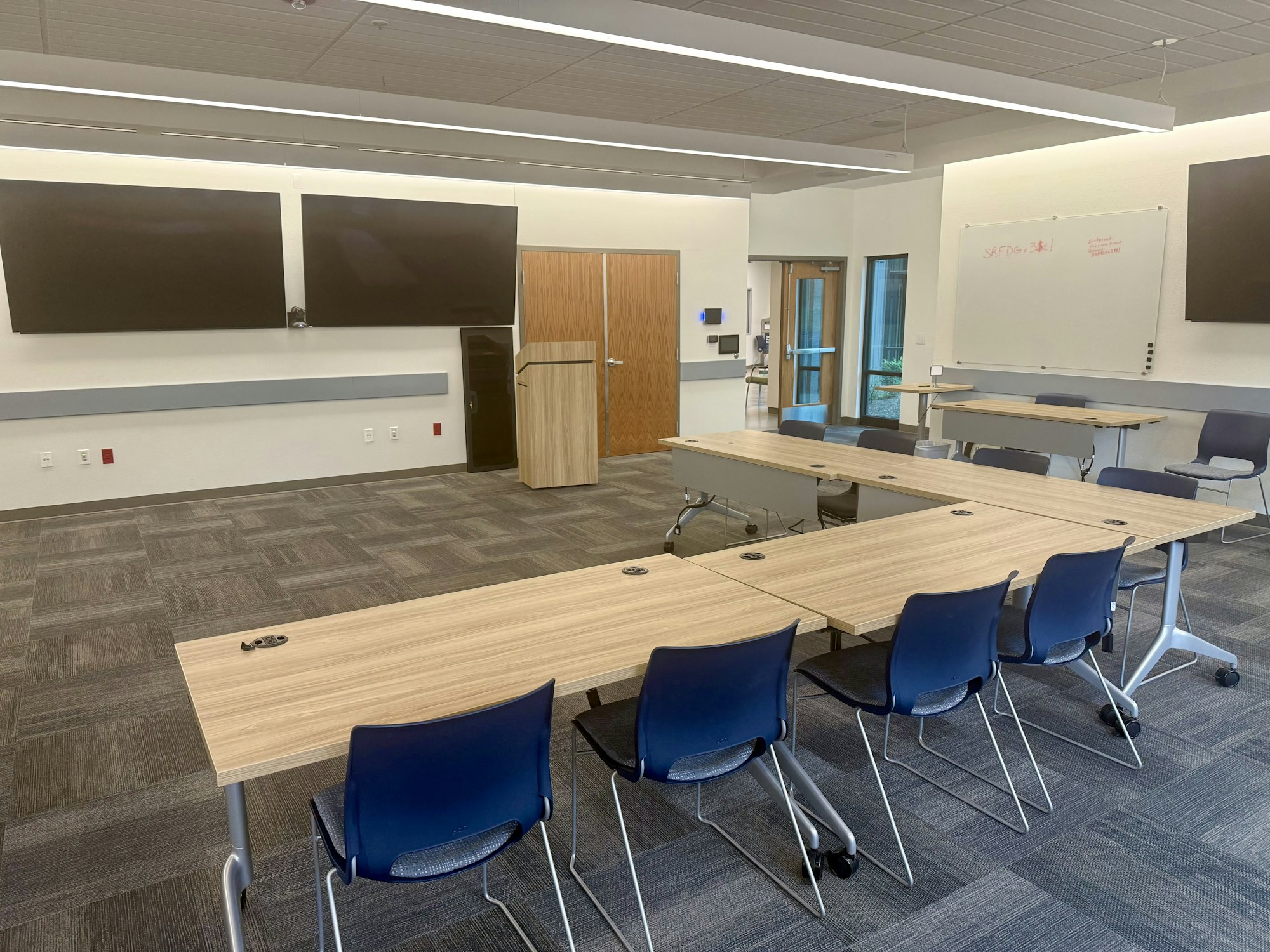 A modern conference room with tables, chairs, large screens, and a whiteboard.