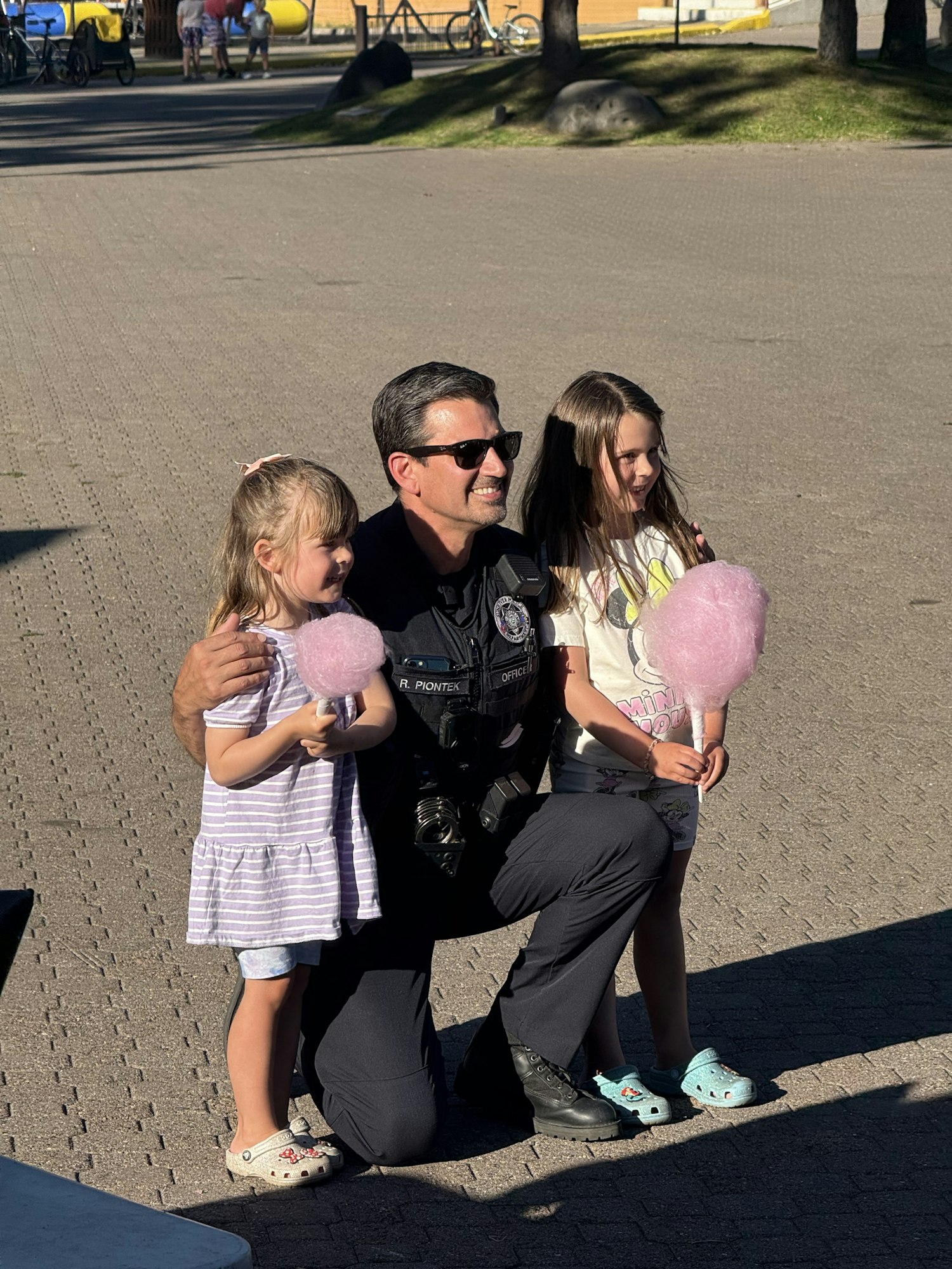 A police officer sitting with two children holding cotton candy.