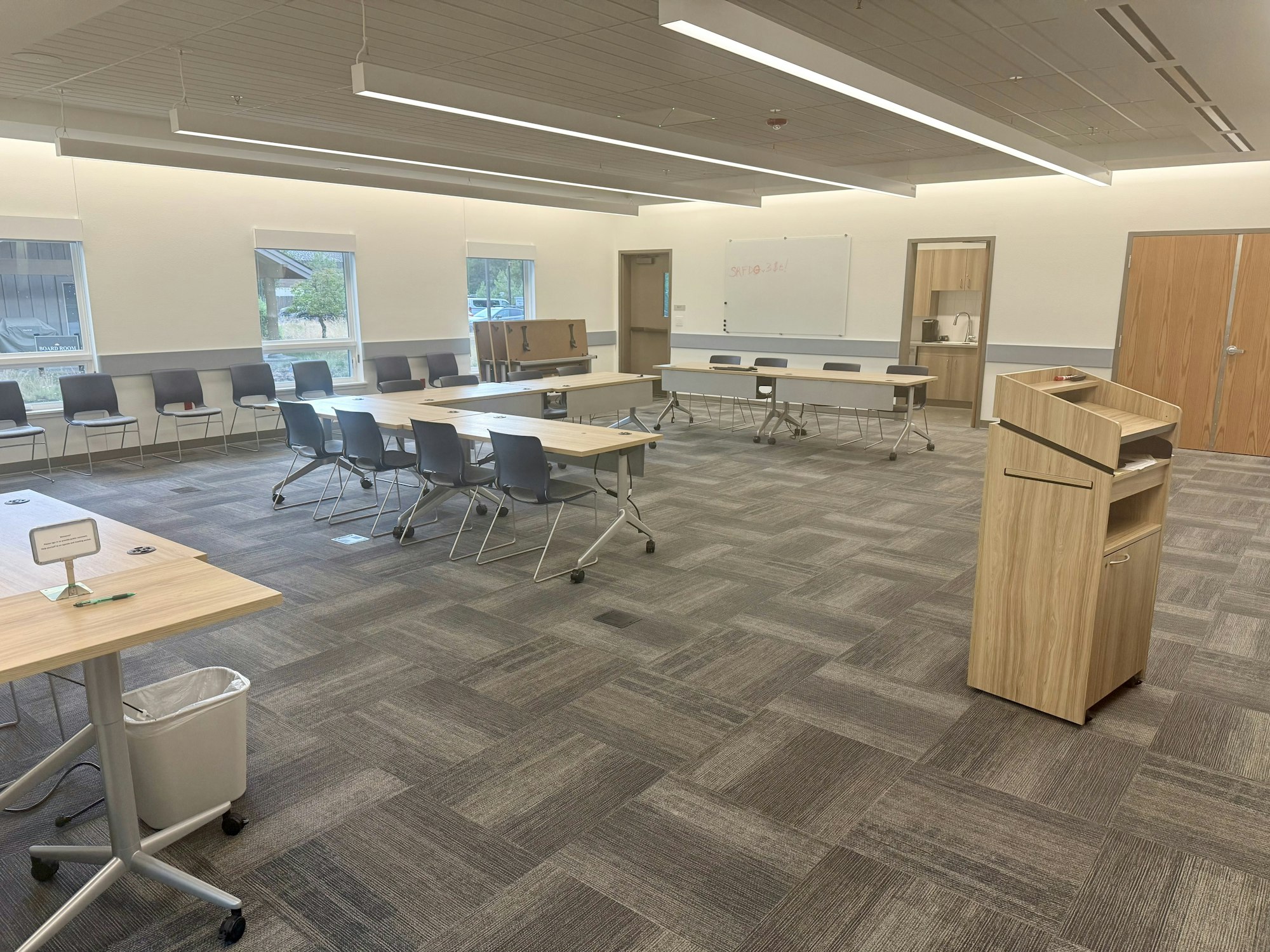 Empty conference room with chairs, tables, a lectern, whiteboard, and windows.