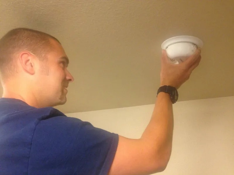 A man is installing a smoke detector on a ceiling.