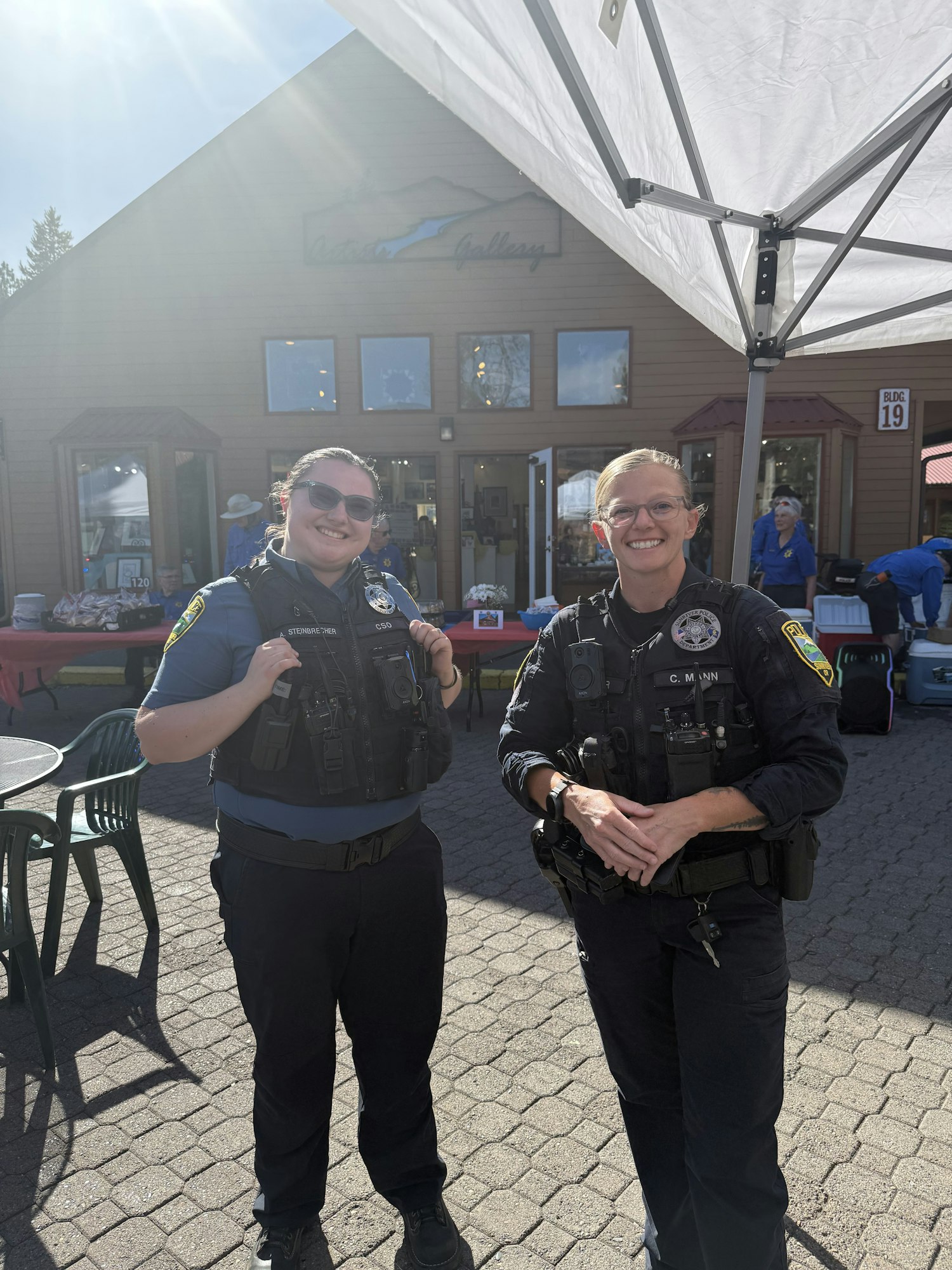 Two police officers smiling under a canopy outside a building.