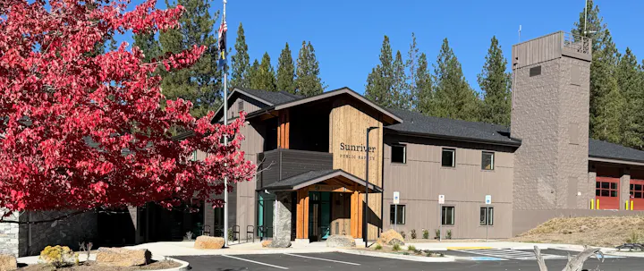 A modern public safety building in Sunriver, surrounded by trees and vibrant red foliage under a clear blue sky.