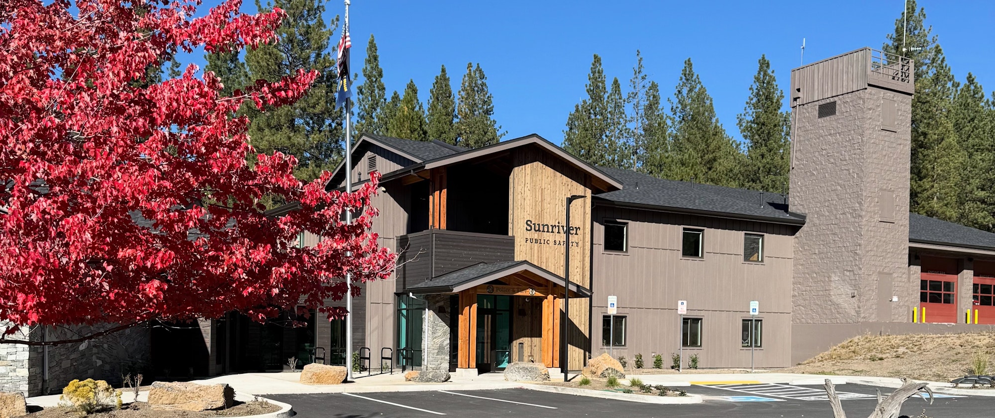 A modern public safety building in Sunriver, surrounded by trees and vibrant red foliage under a clear blue sky.