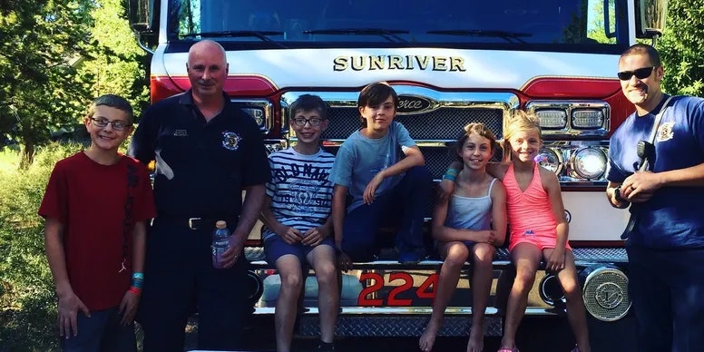 A group of kids with two firefighters in front of a fire truck labeled "SUNRIVER".