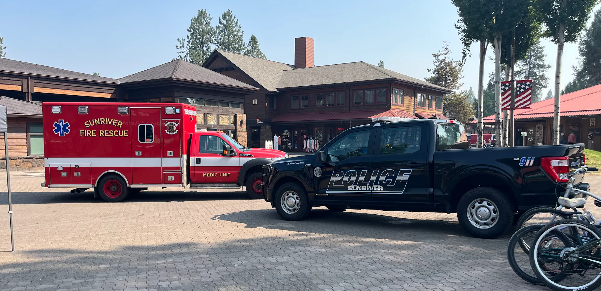 The image shows a red ambulance and a black police truck parked near buildings, likely in a community area.