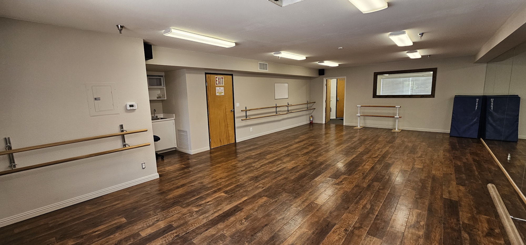 Dance studio with mirrors, ballet barre, wooden floor, and exit door.