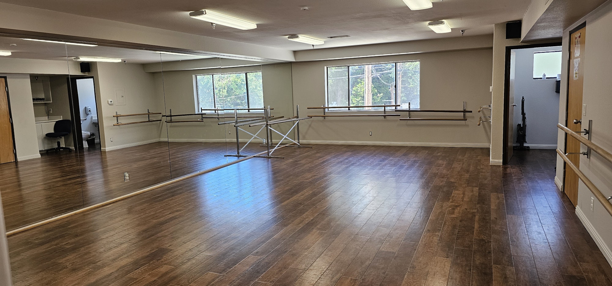 Dance studio with mirrors, wooden floor, ballet barres, and large windows.