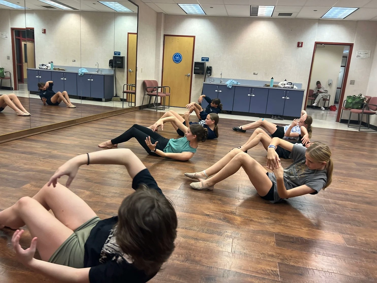 People are practicing dance moves on a wooden floor in a mirrored room.