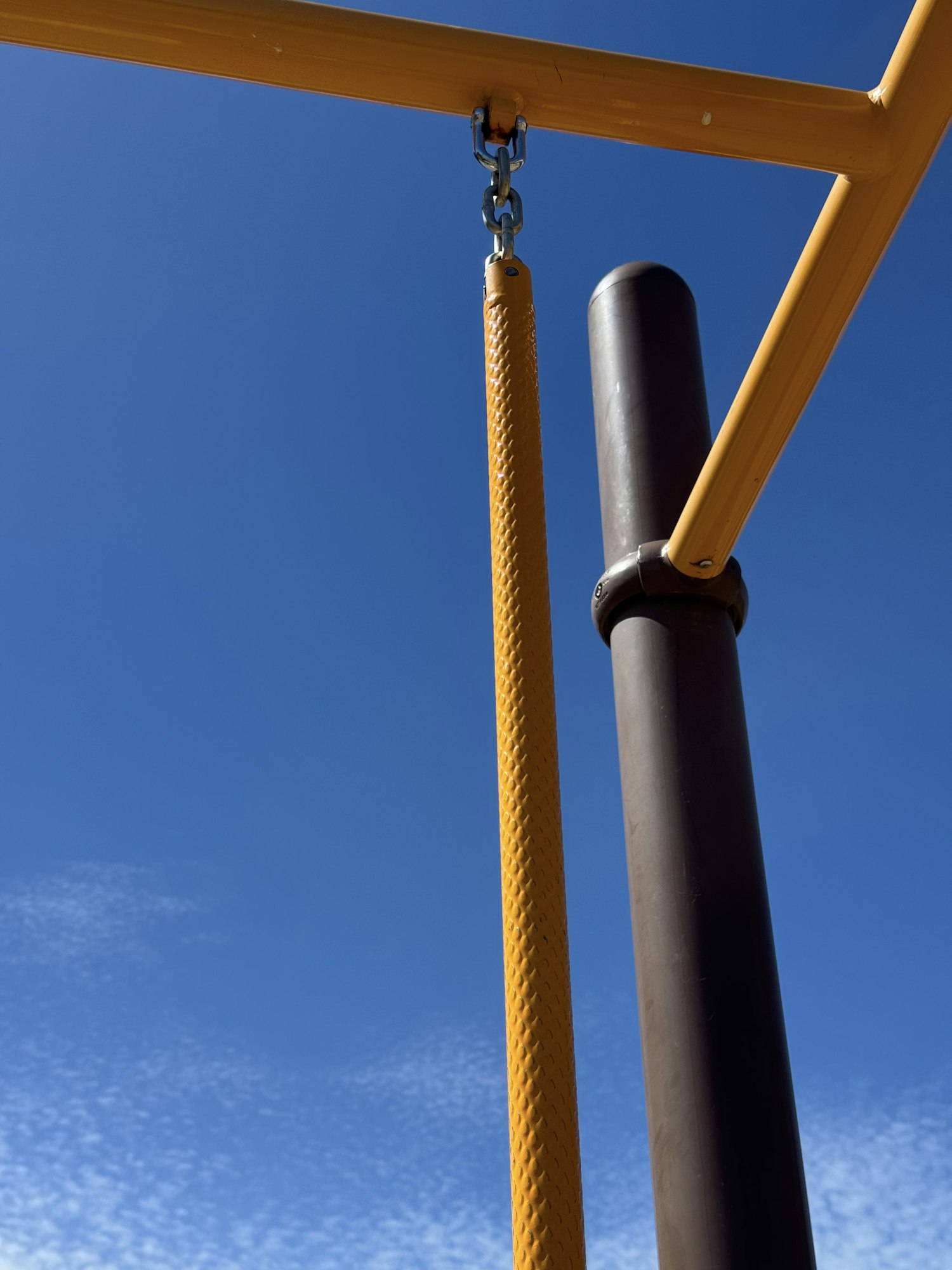 The image shows playground equipment featuring a black pole and a yellow section against a clear blue sky.