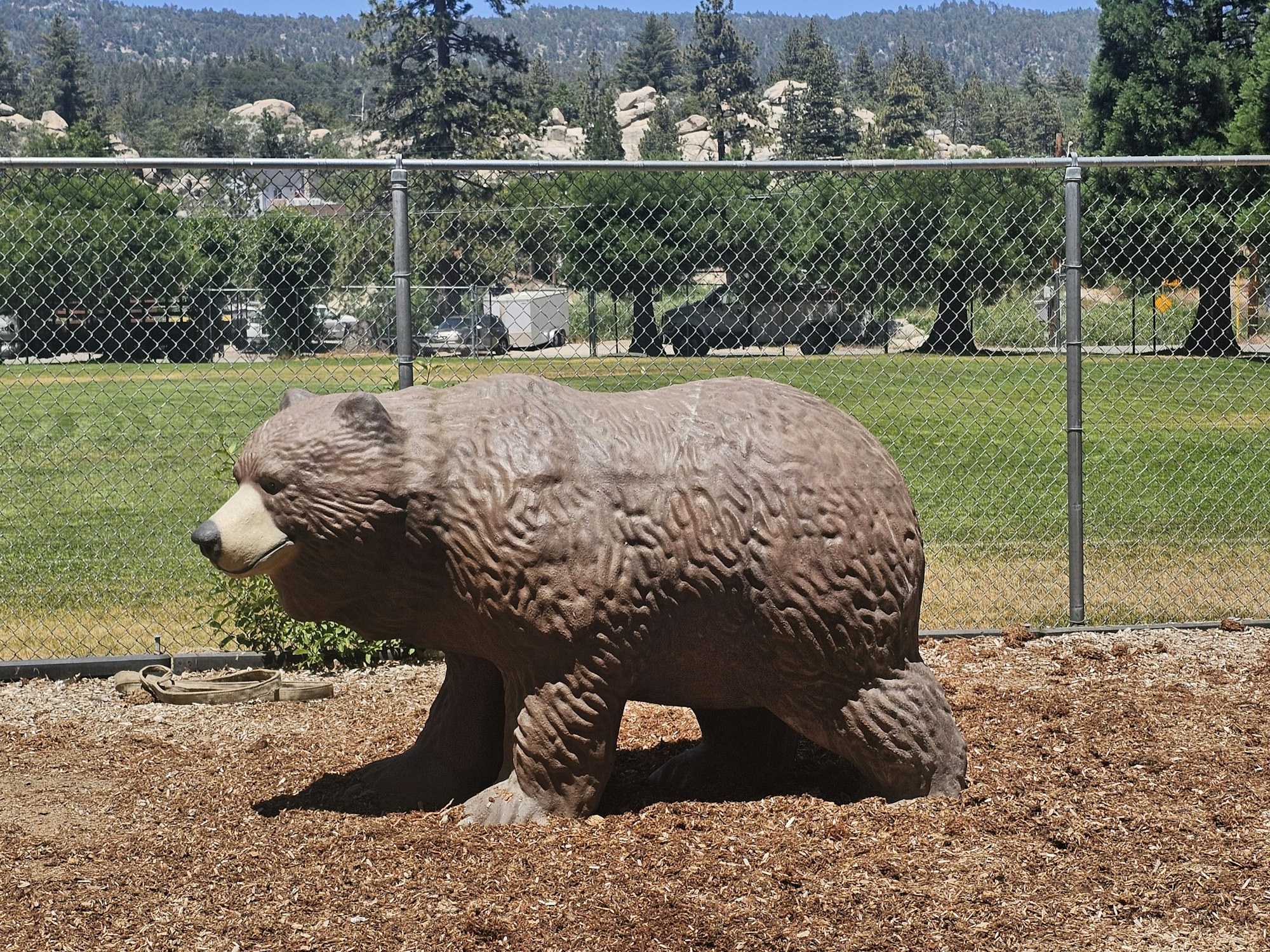 A bear sculpture behind a fence with trees and a clear sky in the background.