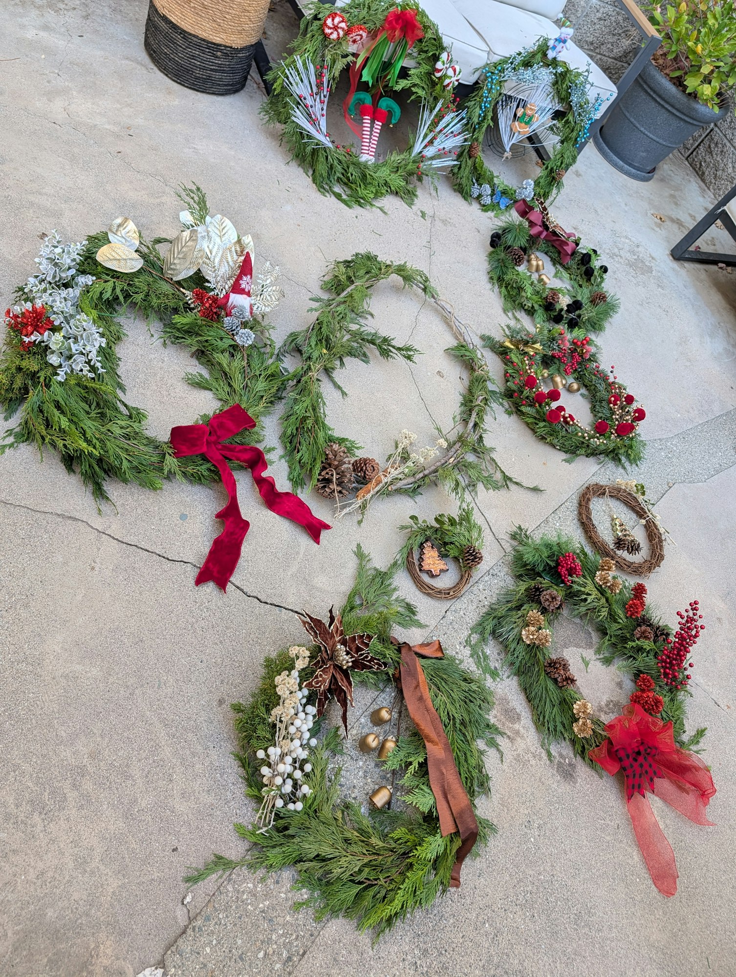 Various decorative Christmas wreaths arranged on the ground, featuring greenery, ribbons, and festive ornaments.