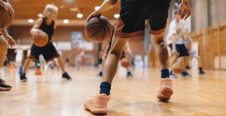 Basketball practice in a gym, focusing on players dribbling and wearing athletic gear.