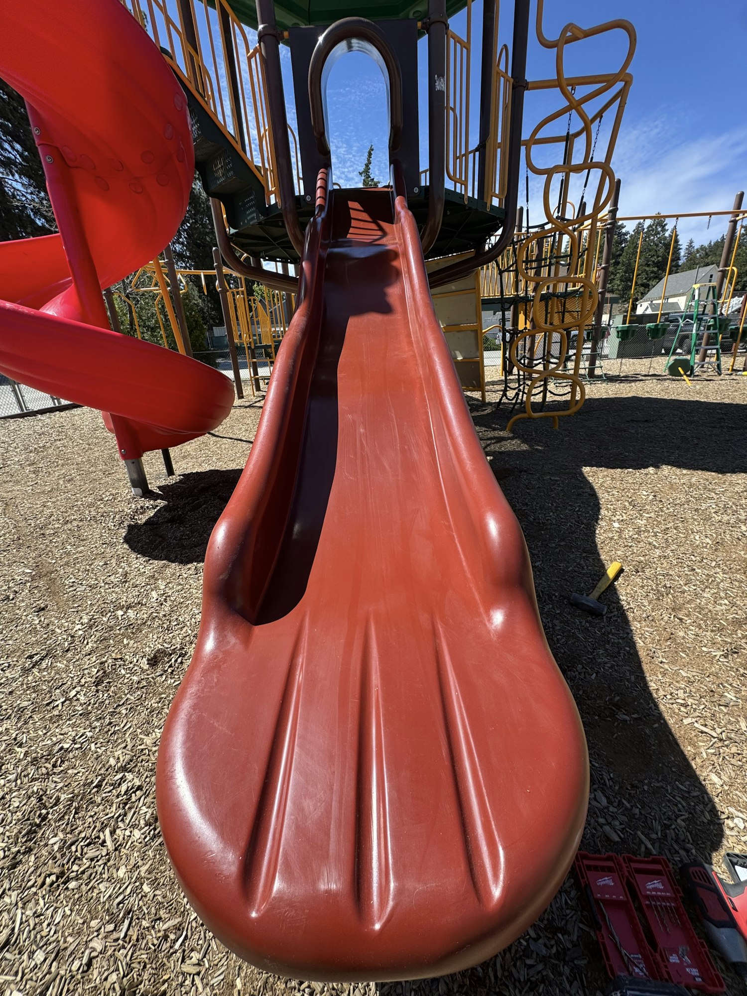 A red slide in a playground with climbing structures and blue sky in the background. Perfect for outdoor fun!