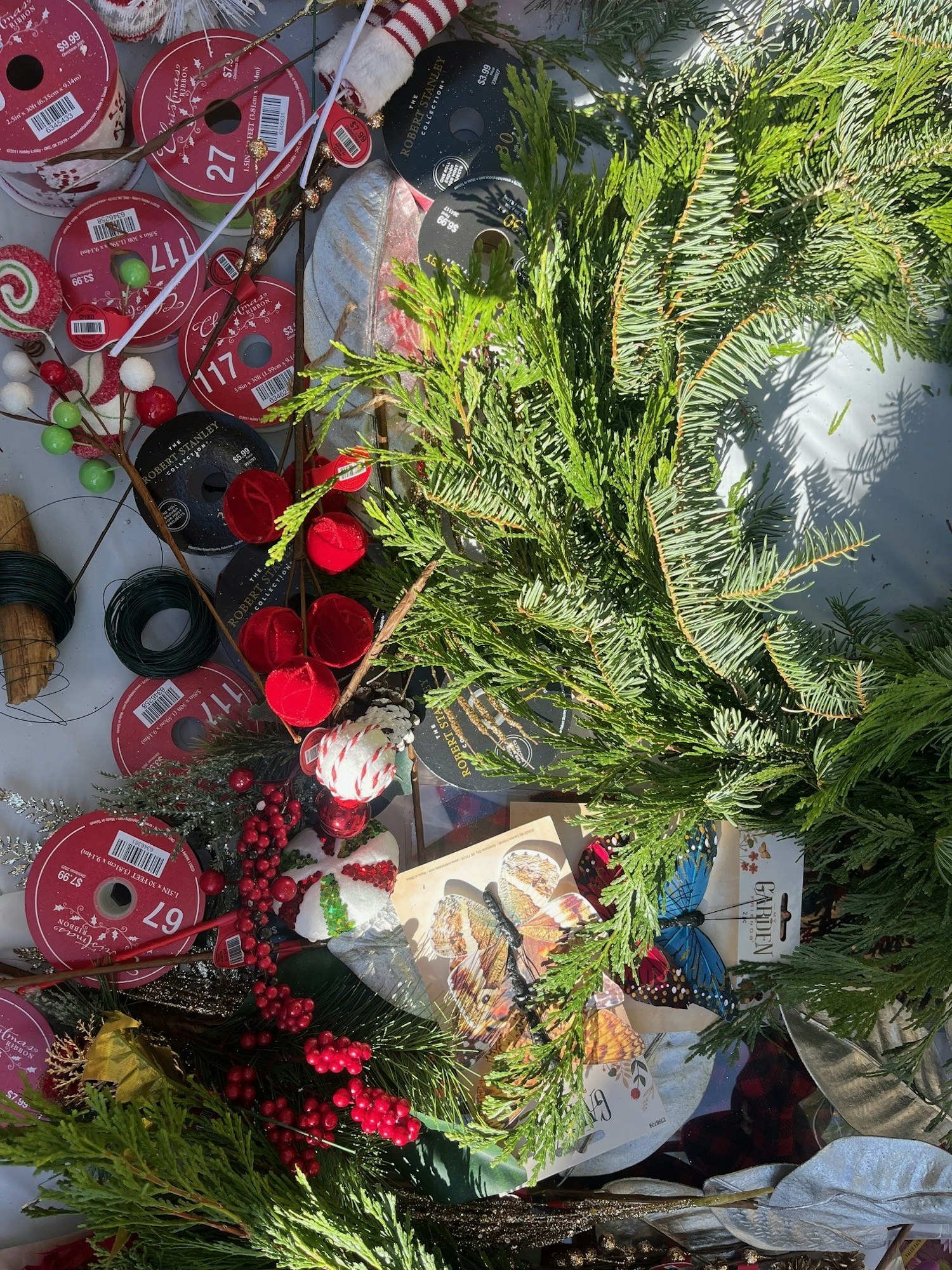 Various ribbons, green branches, red berries, and decorative butterflies on a table, likely for crafting or holiday decorations.