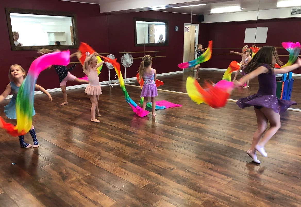 Children dancing with colorful scarves in a studio with mirrors.