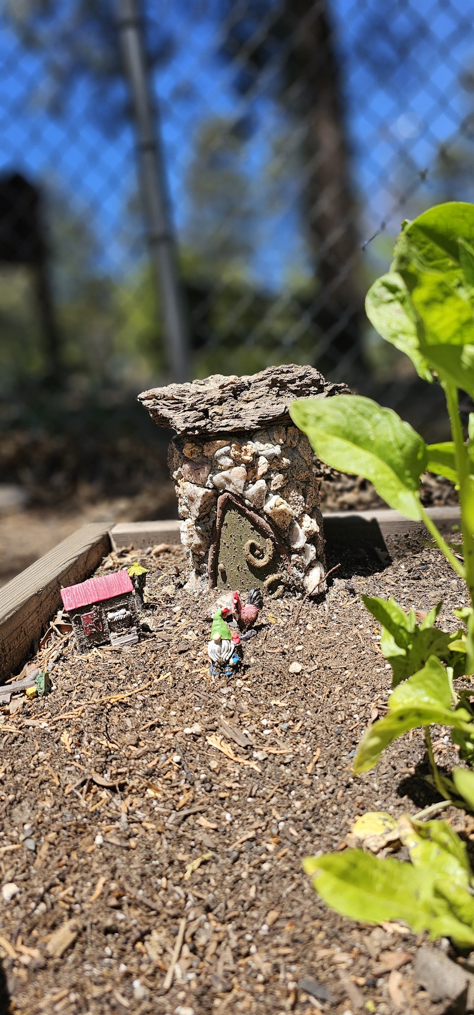 Miniature fairy garden scene with small figures and a rustic house in the soil.