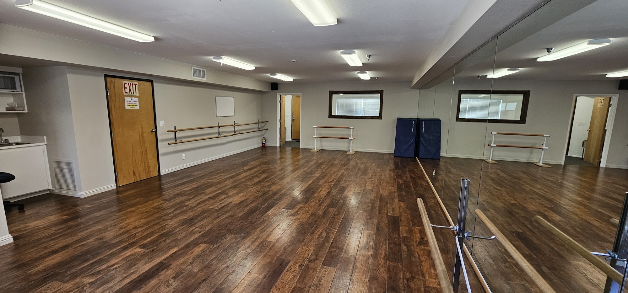 A dance studio with mirrors, wooden floors, ballet barres, and an exit door.