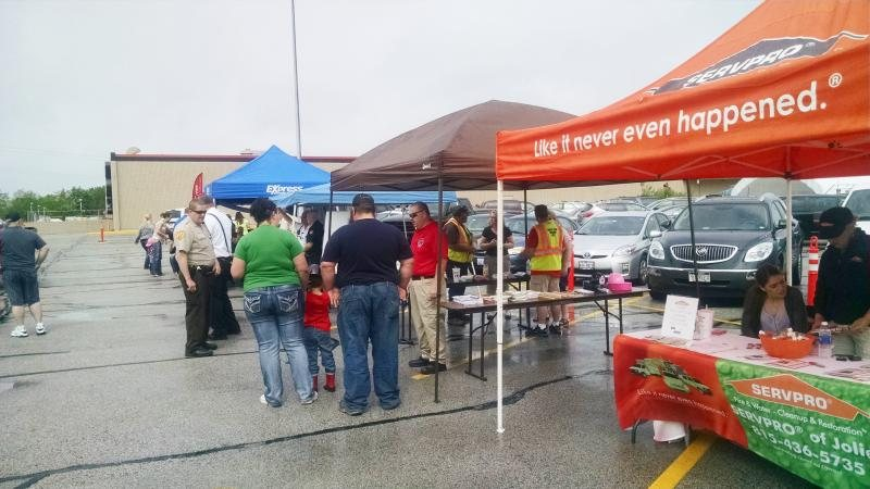 Outdoor event with multiple booths and people gathered under tents in a parking lot.