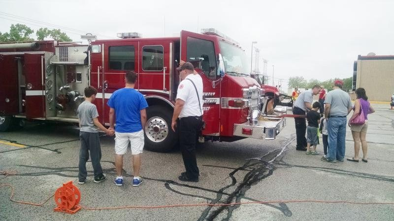 People gathered around a red fire truck in a parking lot, with two children and several adults looking at the vehicle.