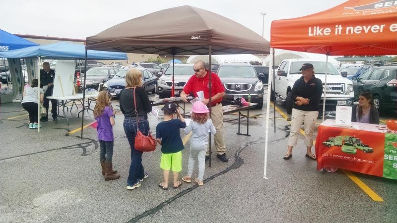 Outdoor event with people at booths, including kids and adults, in a parking lot.