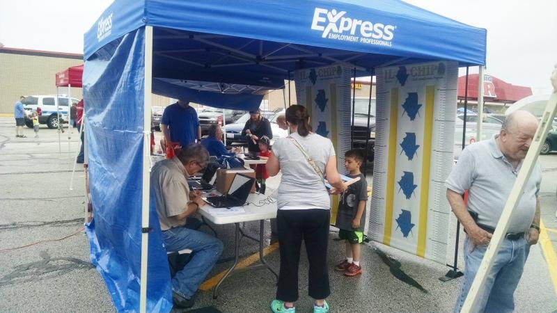 People under a blue tent at a community event, with a sign for Express Employment Professionals.