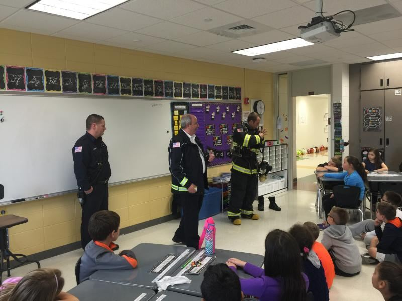 Firefighters giving a safety presentation to young students in a classroom setting.