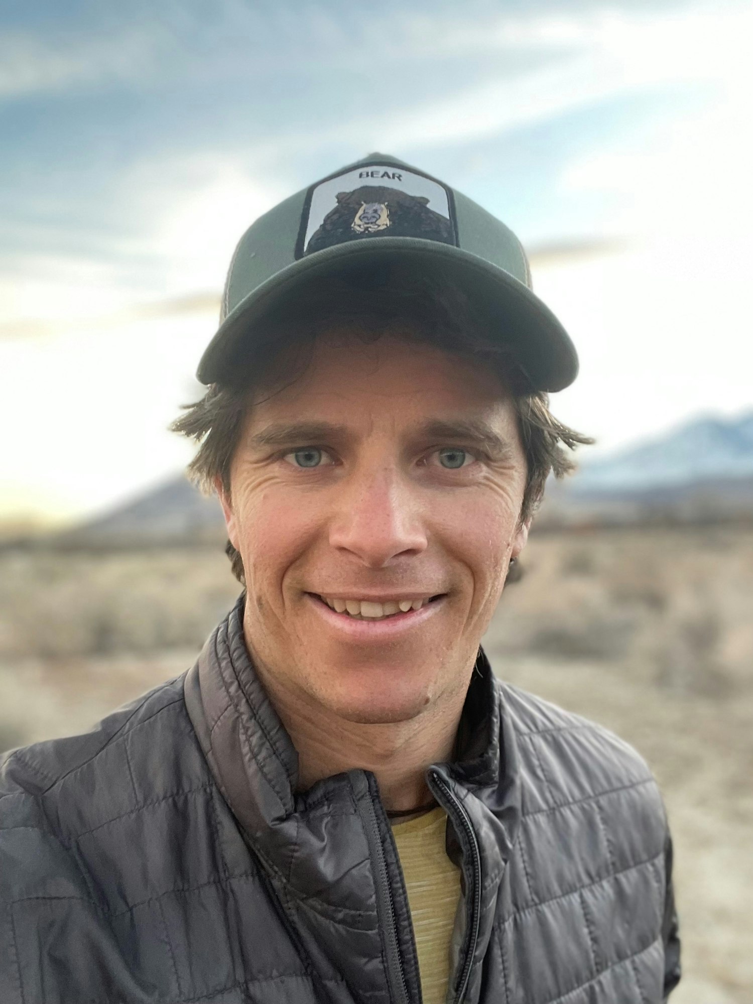 May contain: baseball cap, cap, clothing, coat, hat, jacket, face, head, person, photography, portrait, happy, smile, adult, male, and man
