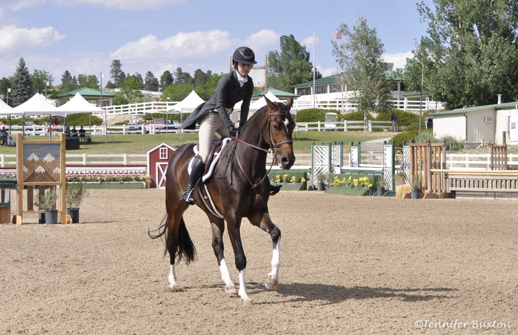 A person riding a horse in an equestrian arena, wearing a helmet and show attire.