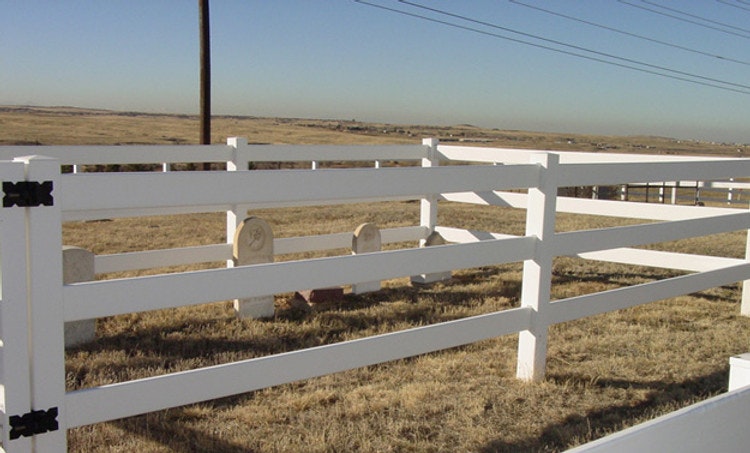 White fence surrounding gravestones on a grassy field with a clear sky.