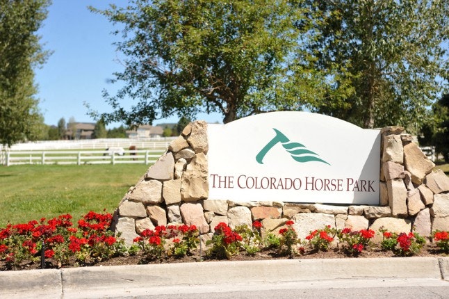 Stone sign for The Colorado Horse Park, surrounded by trees and flowers.
