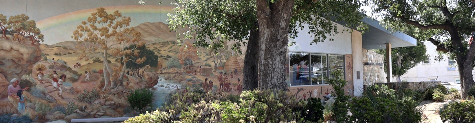 A colorful mural depicts scenes of nature and people, set against a backdrop of trees and a building.