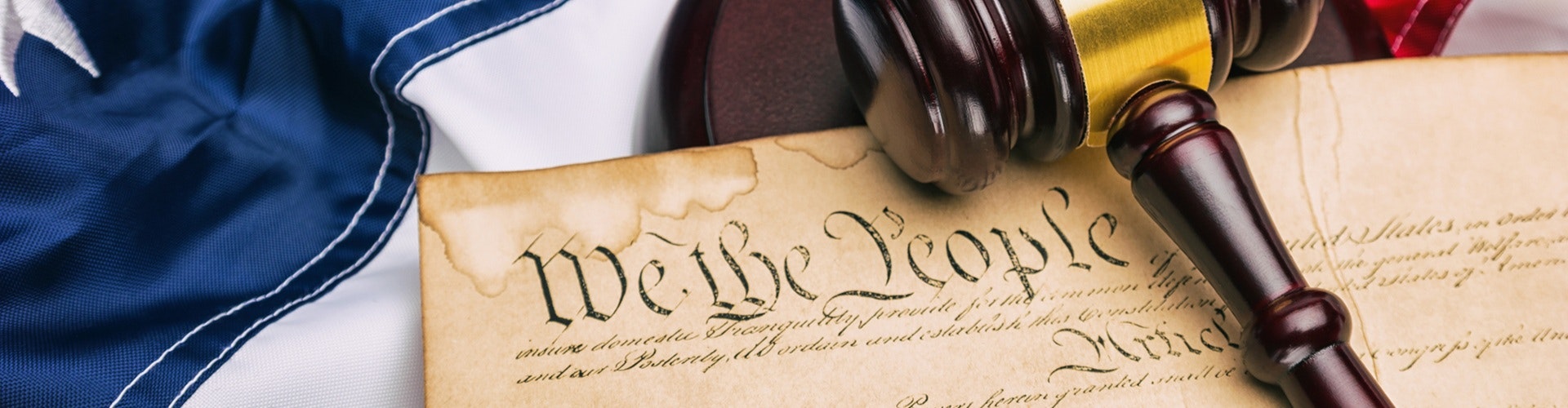 A gavel on a partially visible U.S. flag beside a document with "We the People" written on it.