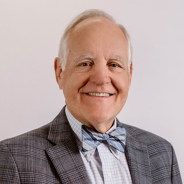 Board Member Bill Clayton wears a formal suit and bowtie smiling at the camera.