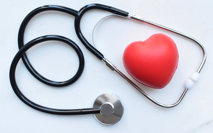 A stethoscope next to a red heart-shaped object on a white surface.