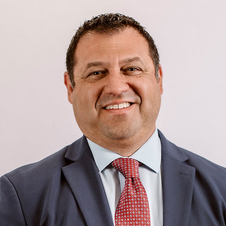 A man in a formal suit and tie smiles at the camera.