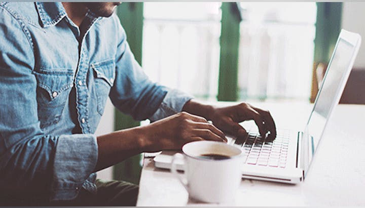 A person using a laptop next to a cup of coffee.